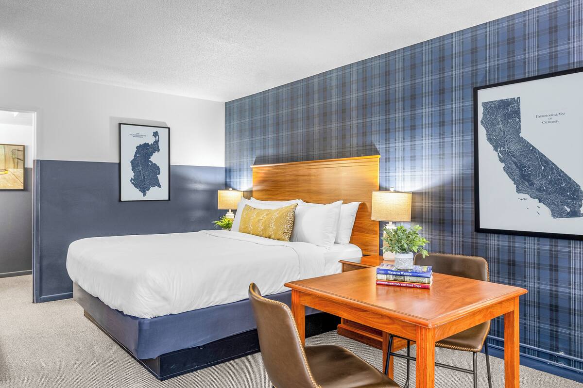 A hotel room with a large bed, a wooden headboard, a desk with a chair, and two wall-mounted lamps.