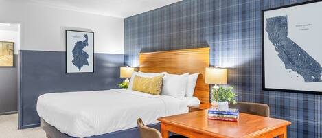Une chambre d’hôtel avec un grand lit, une tête de lit en bois, un bureau avec une chaise et deux lampes fixées au mur.