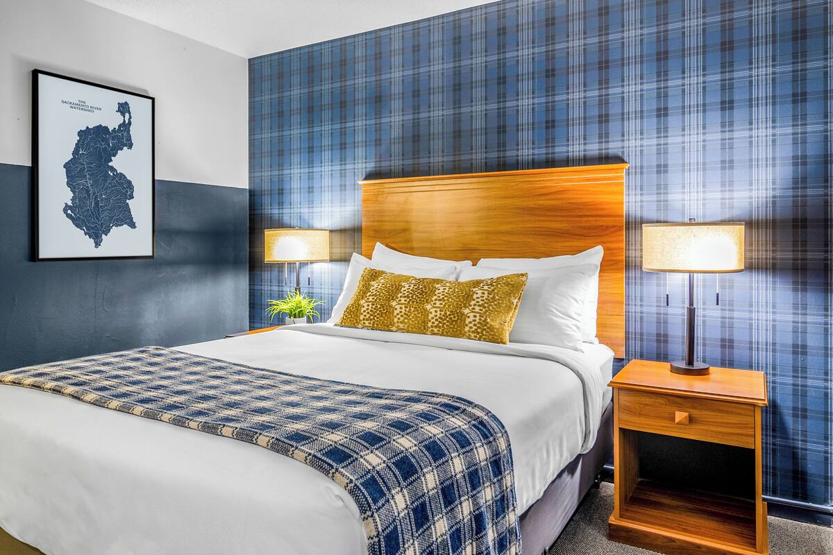 A hotel room with a large bed, two bedside tables with lamps, a map on the wall, and a plaid-patterned wall.