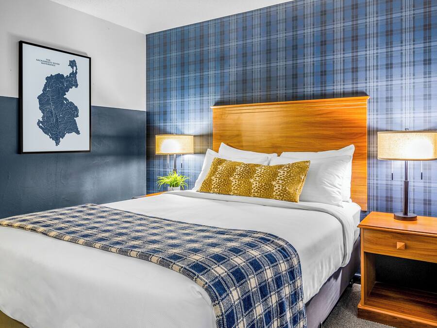 A hotel room with a large bed, two bedside tables with lamps, a map on the wall, and a plaid-patterned wall.