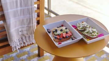 Two square white dishes with fruit and cheese on toast, placed on a round yellow table.