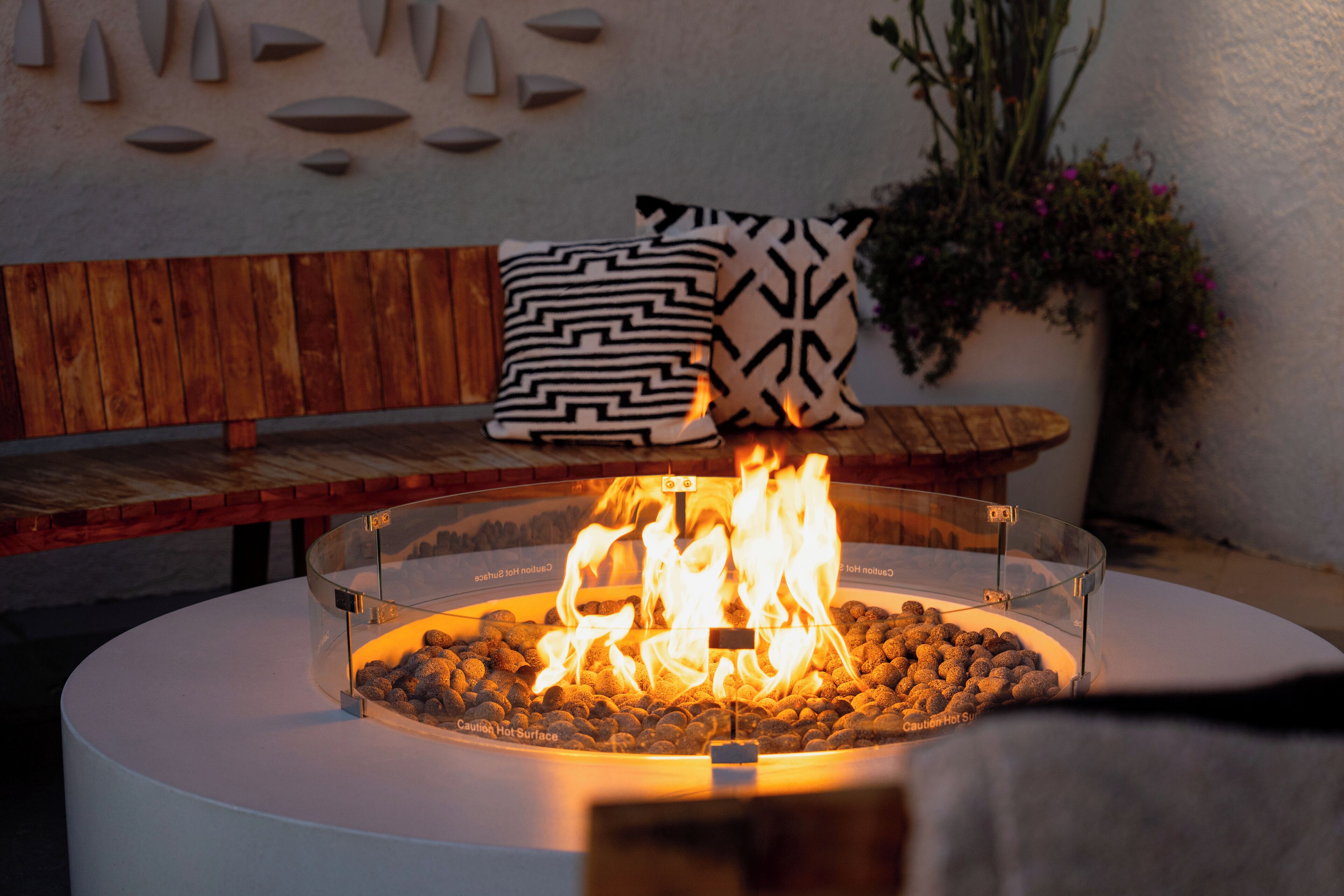 A round outdoor seating area with a fire pit in the center, surrounded by a glass enclosure.