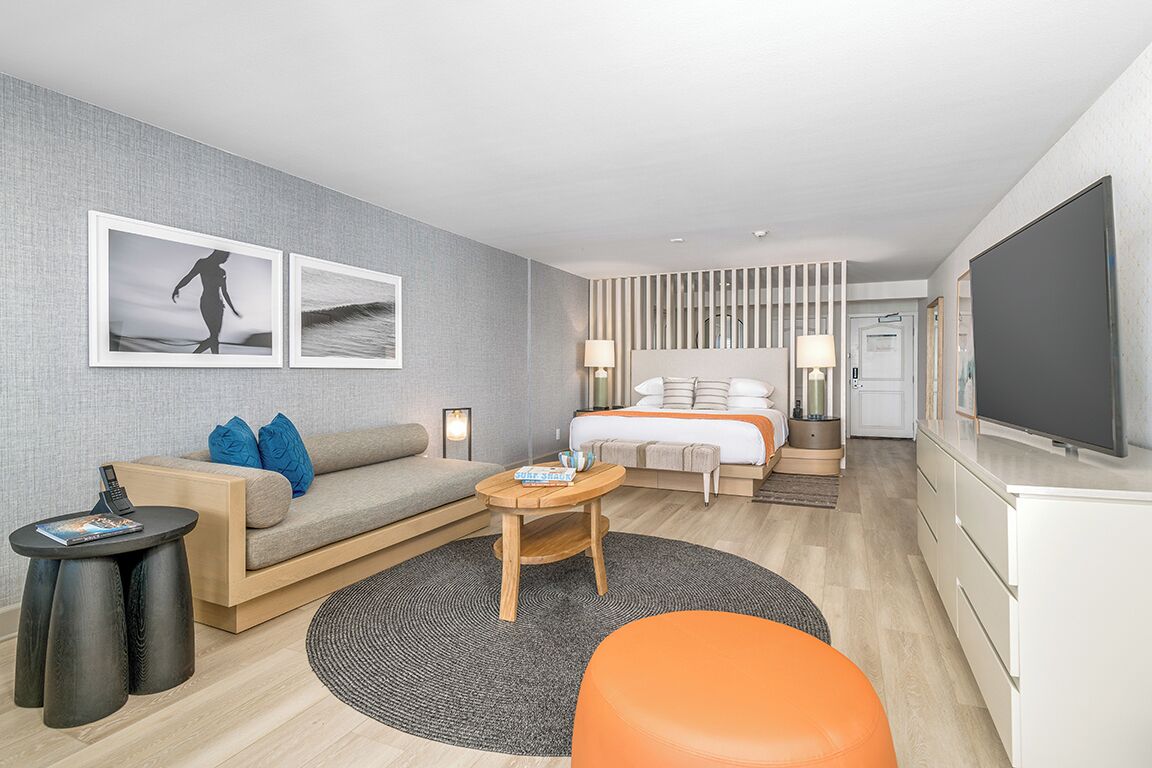 A modern hotel room with a sofa, a bed, a television, and artwork on the wall.