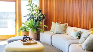A modern living room with a grey sofa, a large potted plant, and a wooden wall.