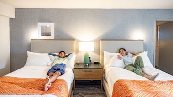 Ein Hotelzimmer mit zwei Betten, jedes mit einer orangefarbenen Musterdecke, einem Nachttisch mit Lampe sowie einem gerahmten Bild an der Wand.