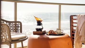 A balcony with a coffee maker, a croissant, and a cup on a round ottoman.
