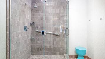 Un baño moderno con ducha envuelta en cristal, inodoro azul y paredes con azulejos.