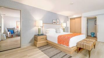 A modern hotel room with a large bed, bedside tables, a bench, and a view of the hallway.