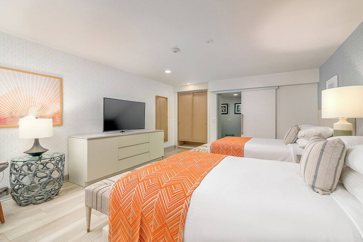 A hotel room with two beds, a TV, a desk, and a lamp.