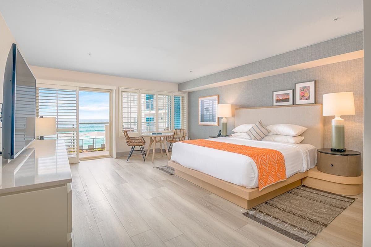 A hotel room with a large bed, a desk, and a view of the ocean through the windows.