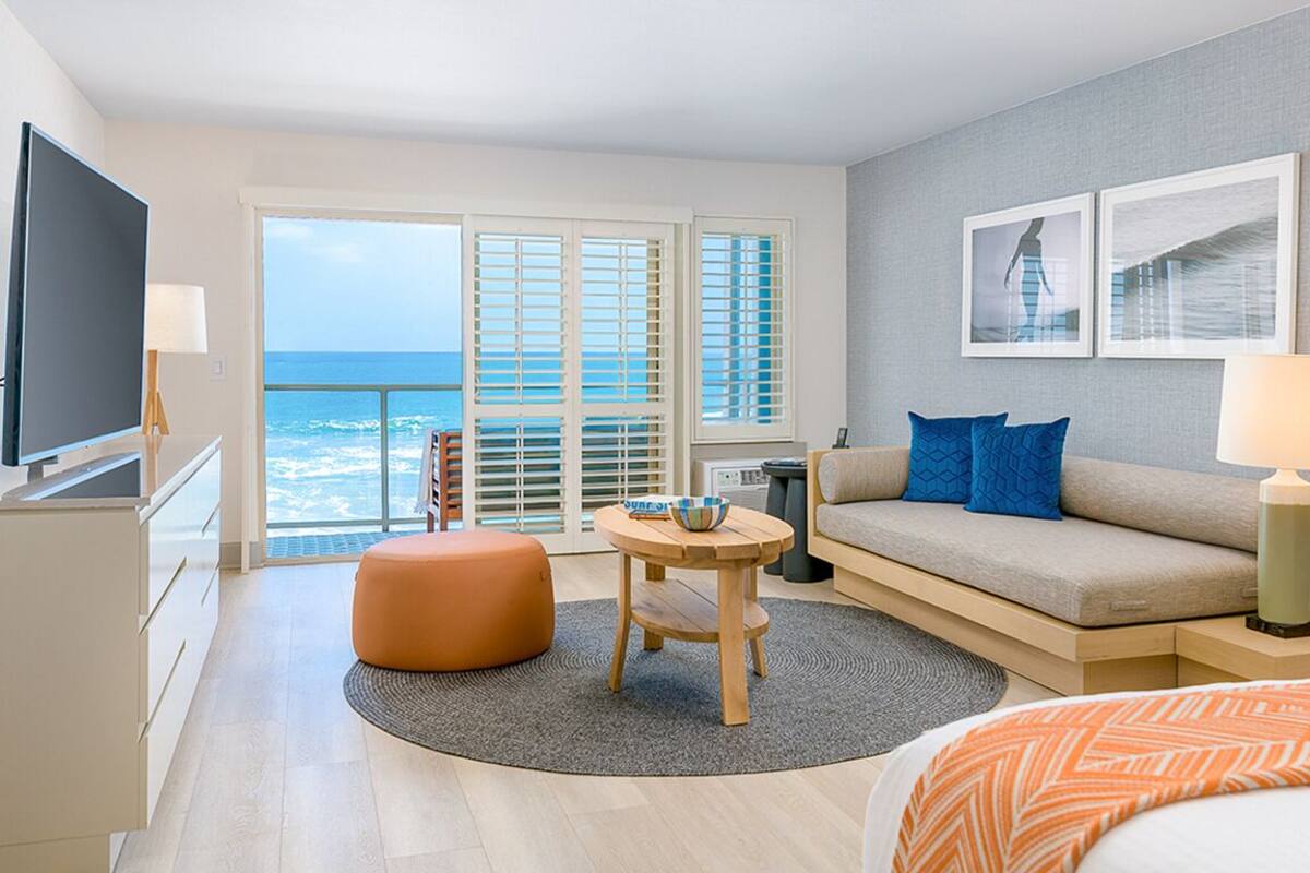 A modern hotel room with a balcony, a sofa, a TV, and a bed.