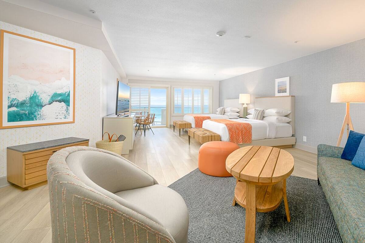 A modern hotel room with a bed, seating area, and a view of the ocean.