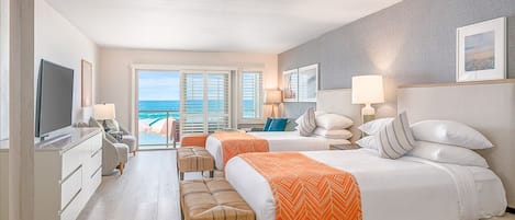 A hotel room with a large bed, two bedside tables, a TV, a desk, and a view of the ocean through large windows.