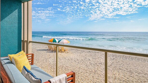 A balcony with a view of the beach and ocean, featuring a sofa with cushions and a table with an umbrella. - Beach Terrace (Carlsbad)