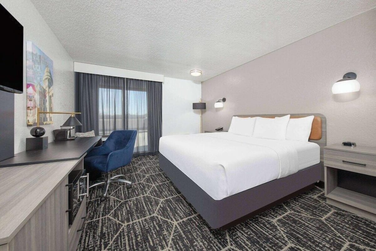 A hotel room with a bed, a desk, a chair, a TV, and a window with curtains.