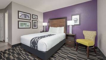 A hotel room with a bed, a chair, and a nightstand with a lamp.