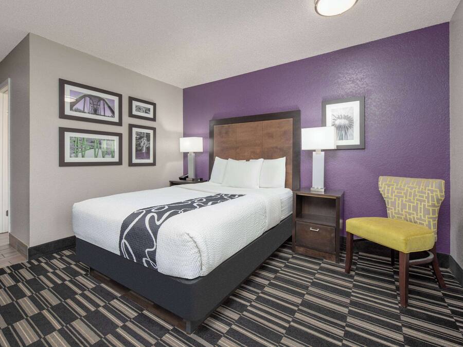 A hotel room with a bed, a chair, and a nightstand with a lamp.