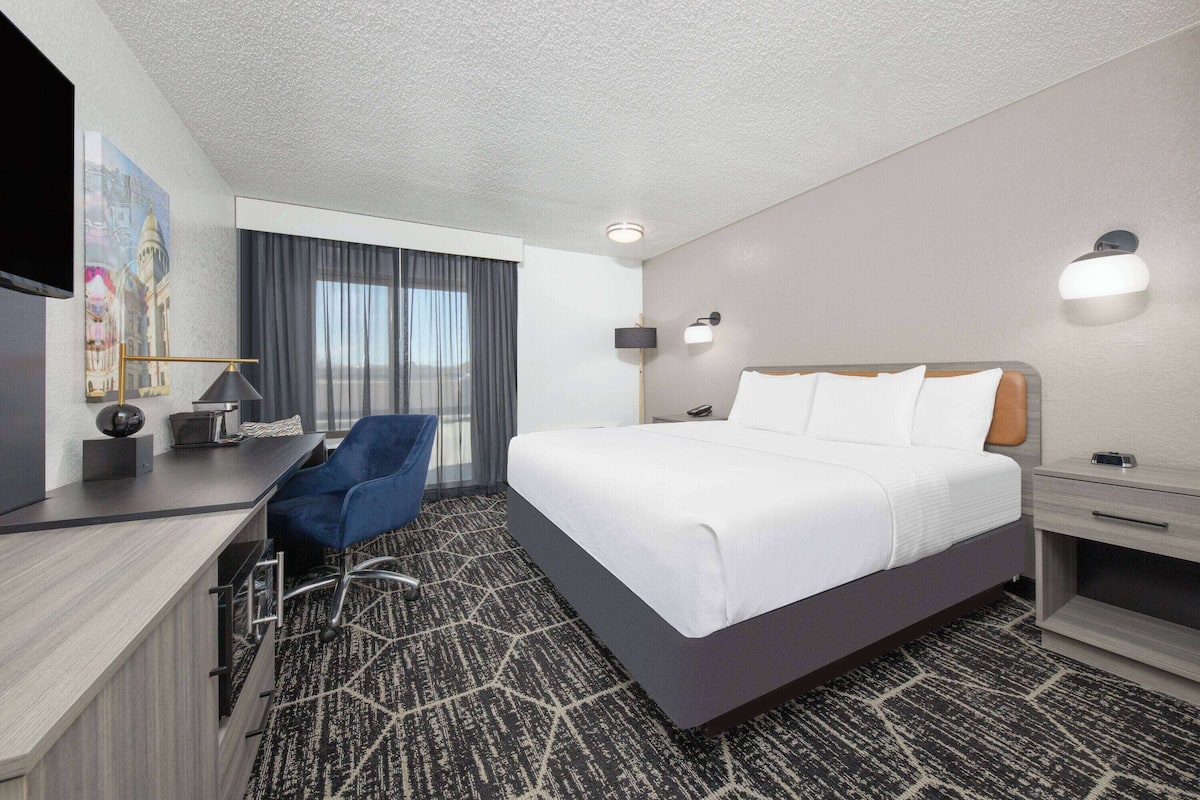 A hotel room with a large bed, a desk with a chair, a TV, and a window with curtains.