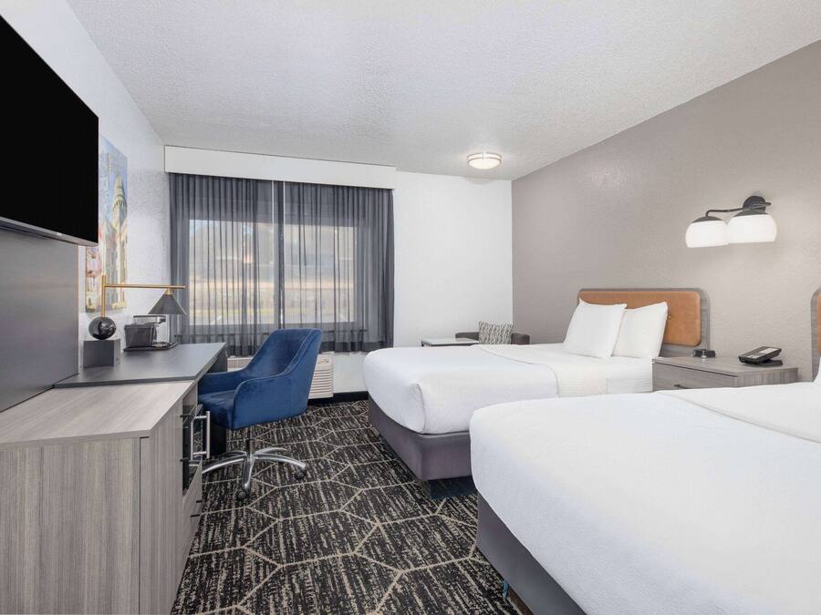 A hotel room with two beds, a desk, a chair, a TV, and a window with curtains.