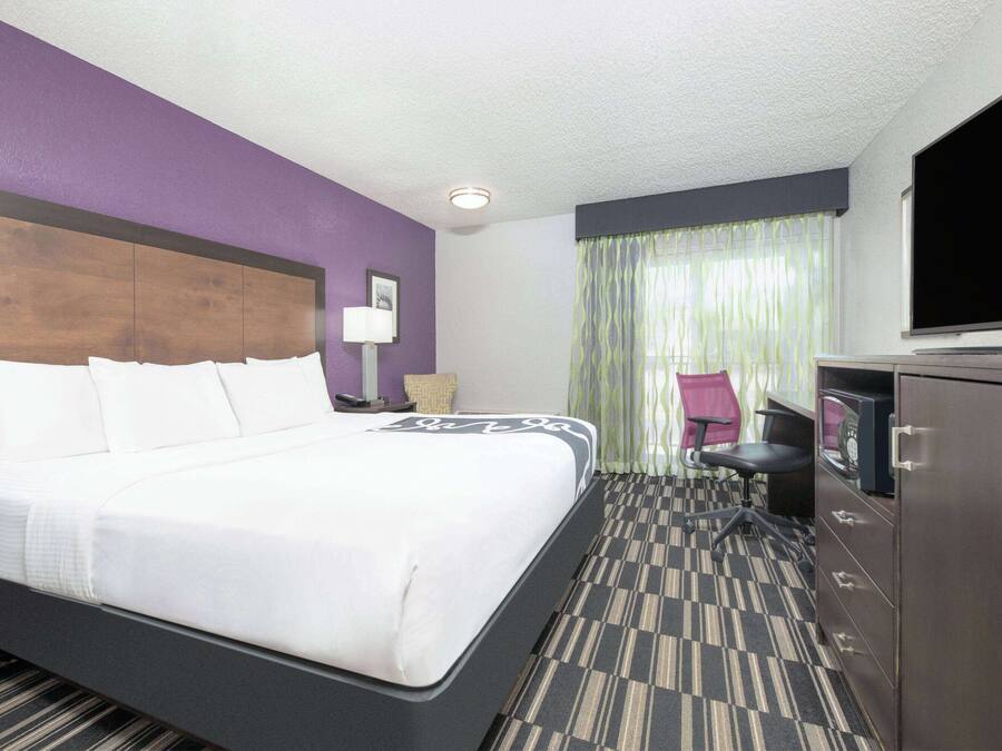 A hotel room with a large bed, a desk with a computer, a TV, and a chair.