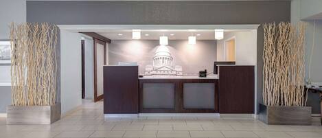 A reception area with a modern design, featuring a reception desk, a decorative wall with a building silhouette, and tall decorative plants.