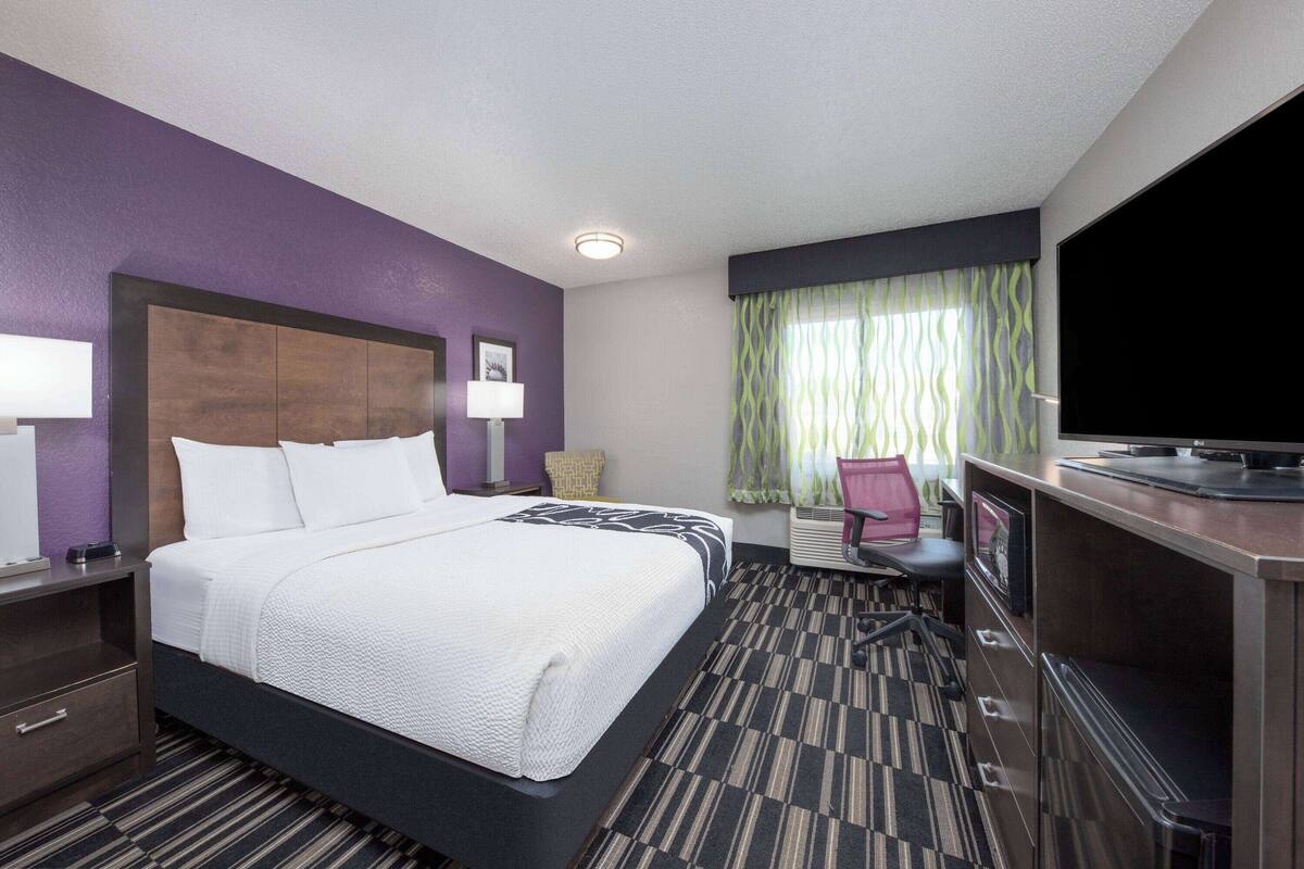 A hotel room with a large bed, a desk with a television, and a chair.