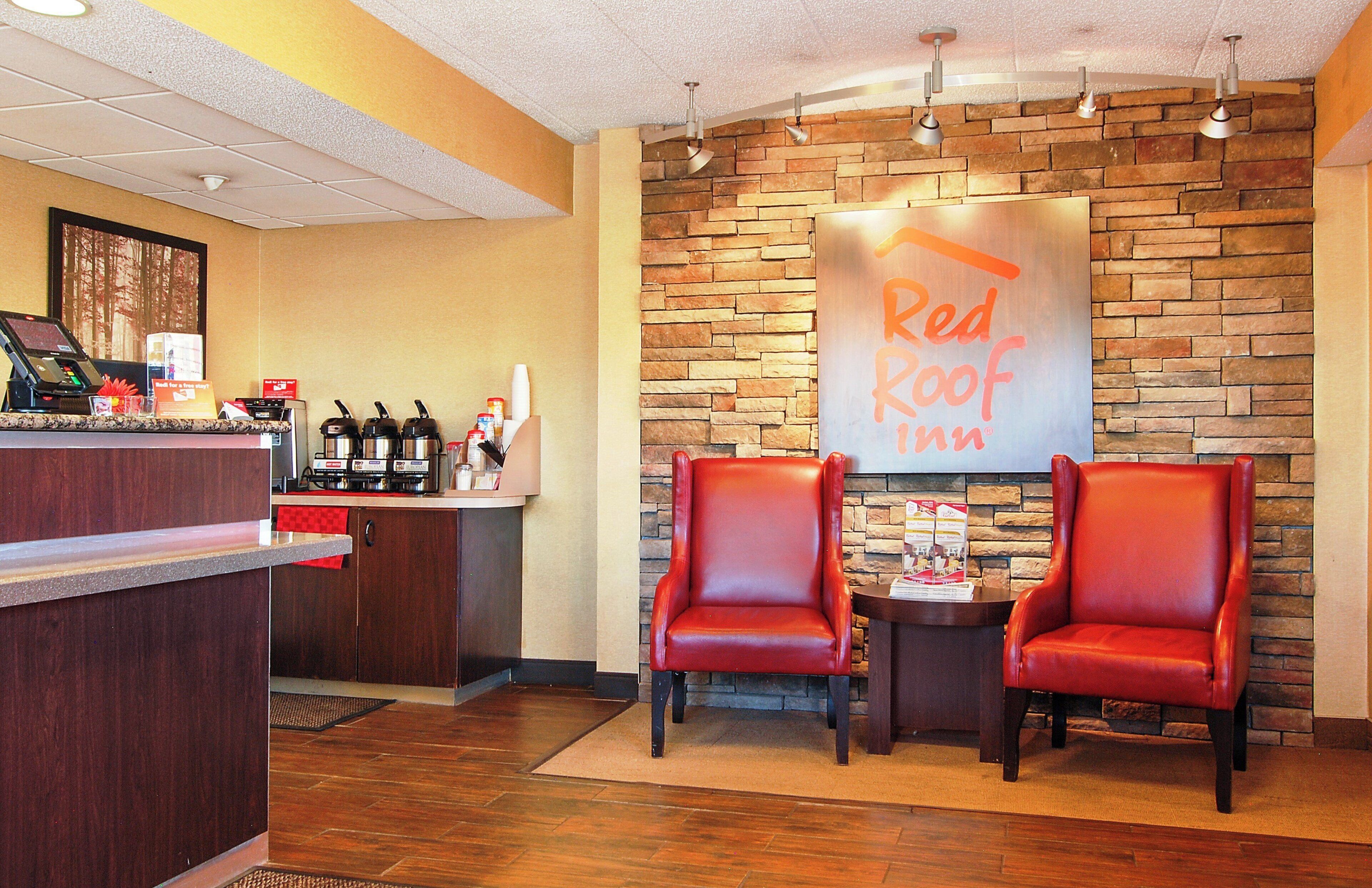 A Red Roof Inn reception area with a brick wall, a counter with a coffee machine, and two leather chairs.