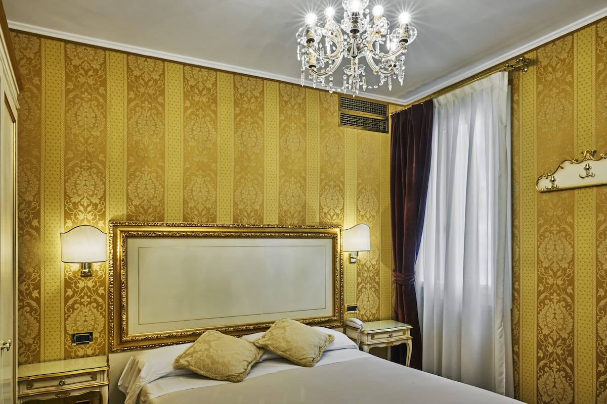 Una lujosa habitación de hotel con una cama grande, papel tapiz dorado ornamentado, una araña y un diseño clásico.