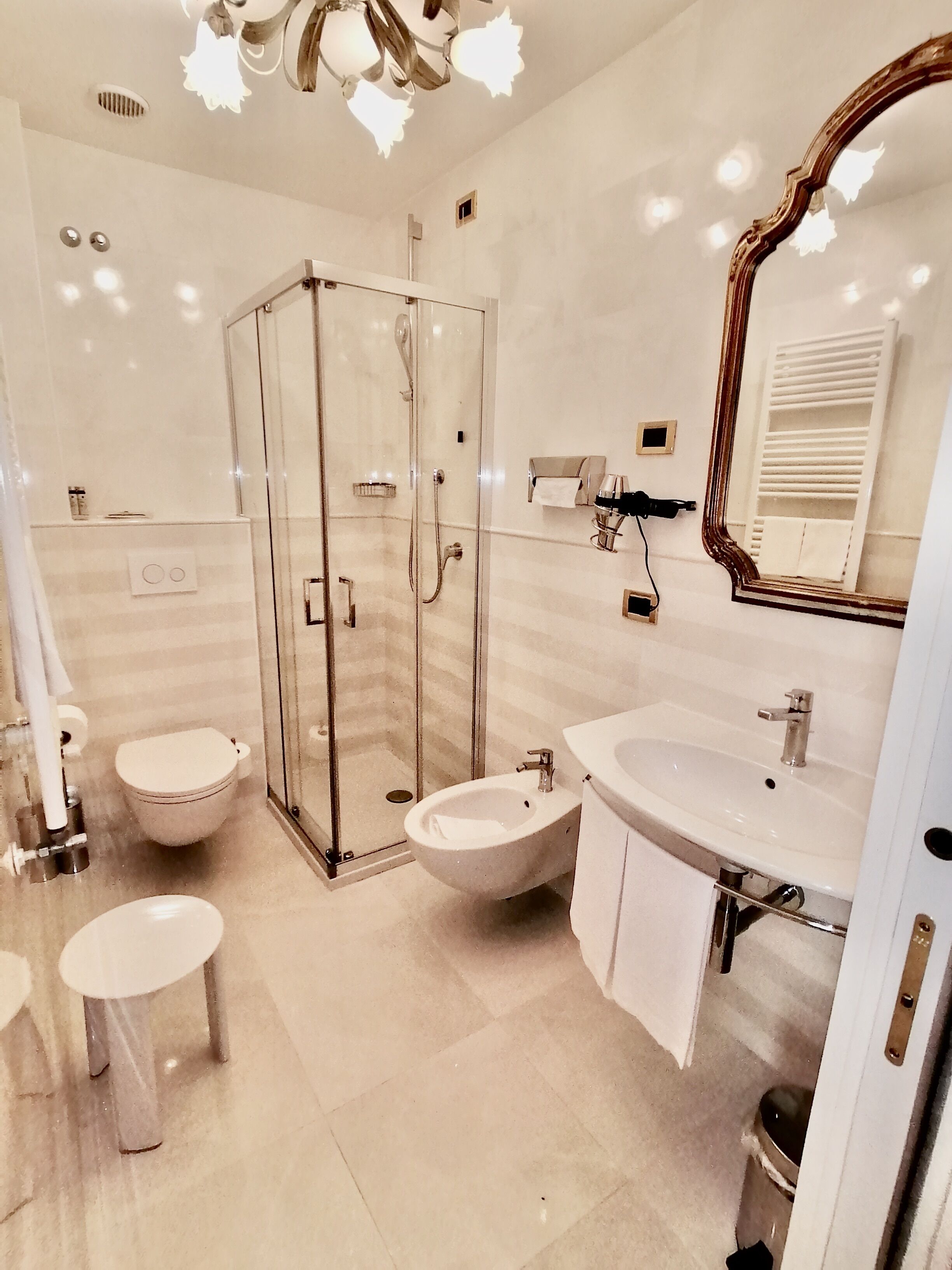 Un baño moderno con ducha envuelta en vidrio, un lavamanos, dos inodoros y un espejo grande.