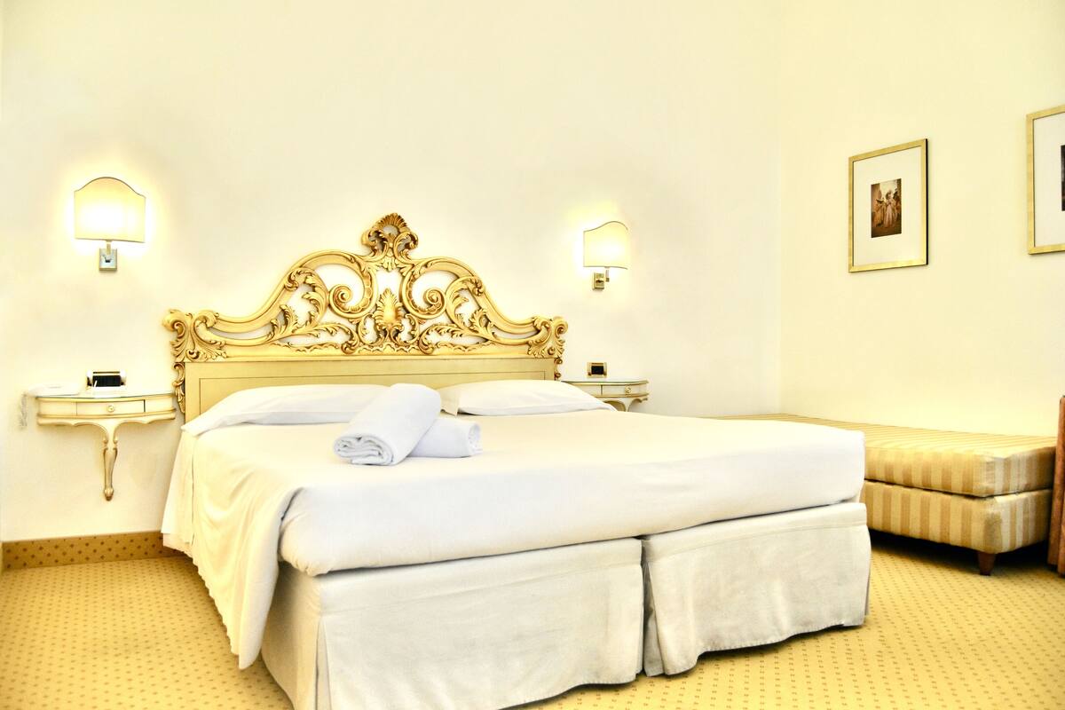 Una habitación de hotel con una cama grande, dos mesitas de noche y una mesita auxiliar.