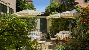 Un patio al aire libre con mesas y sillas, rodeado de abundante vegetación y cubierto por sombrillas grandes.