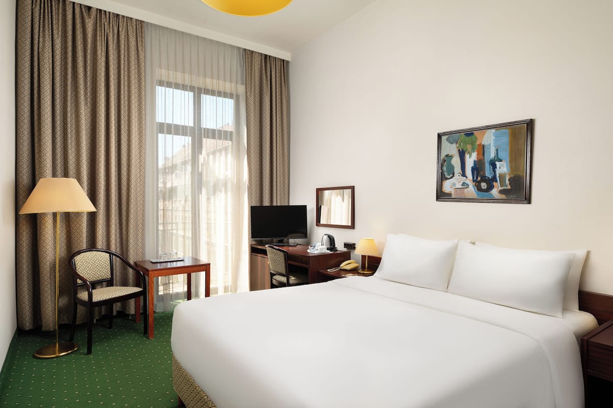 Habitación de hotel con una cama grande, un escritorio con computadora, una silla, un televisor y un cuadro en la pared.