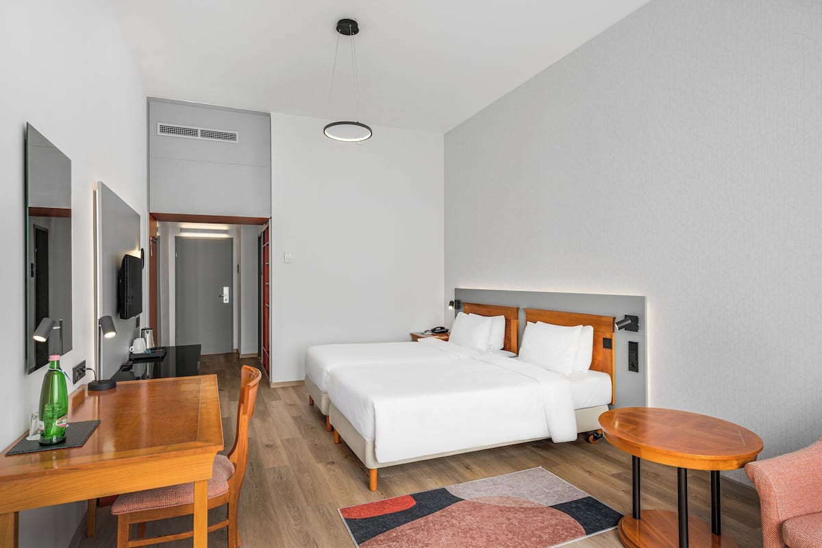 Una habitación de hotel con cama, mesita de noche, silla y una pequeña mesa redonda.