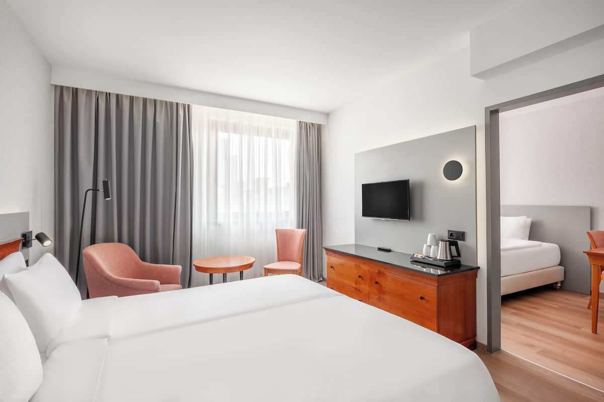 Una habitación de hotel con una cama grande, un escritorio con televisión de pantalla plana, una silla, una mesita y un armario.