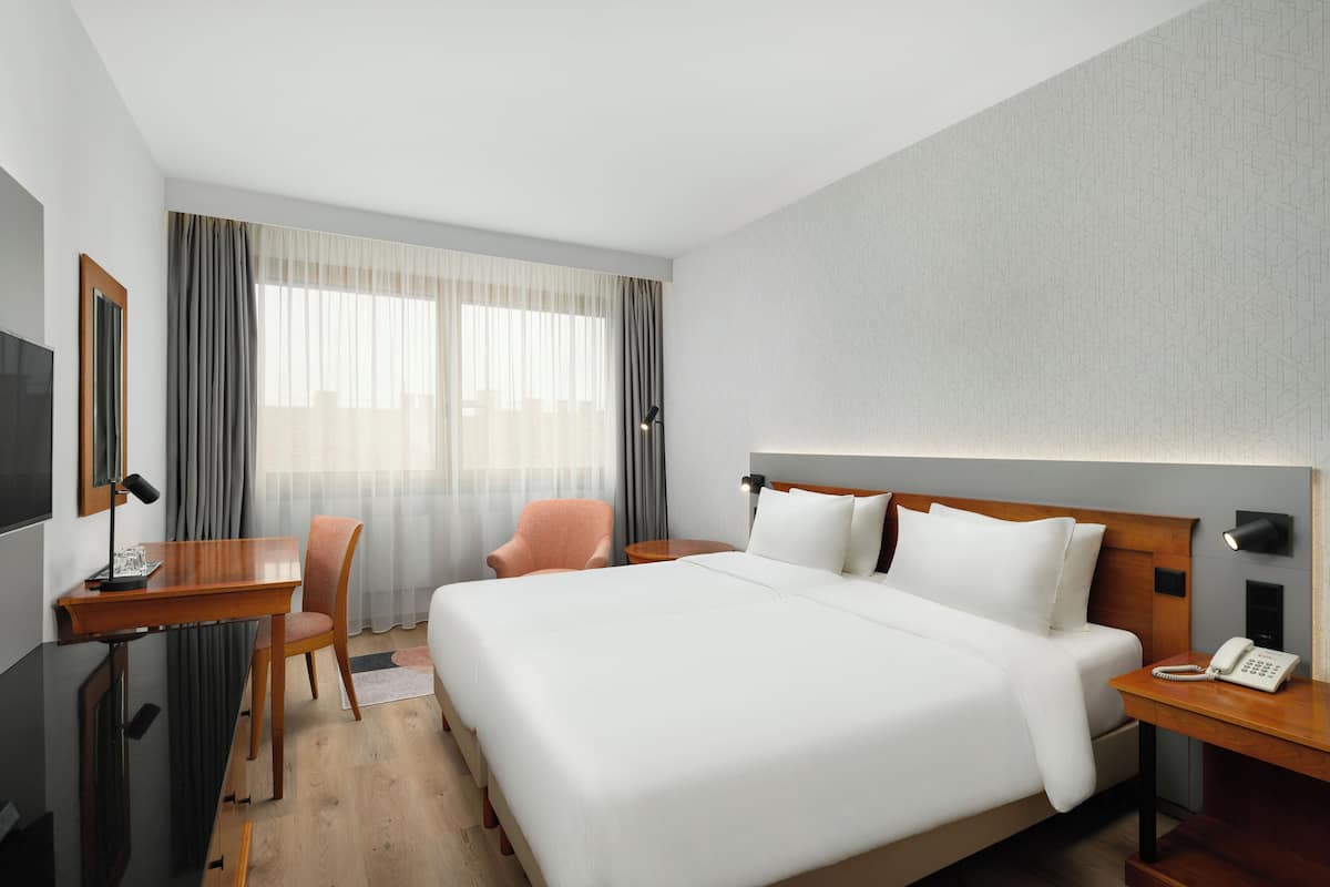 Una habitación de hotel con una cama grande, un escritorio con silla, un televisor y un teléfono en la mesita de noche.