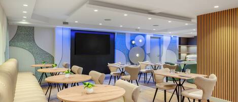 Un espace de détente moderne avec des tables rondes, des sièges confortables et un grand écran pour les présentations.