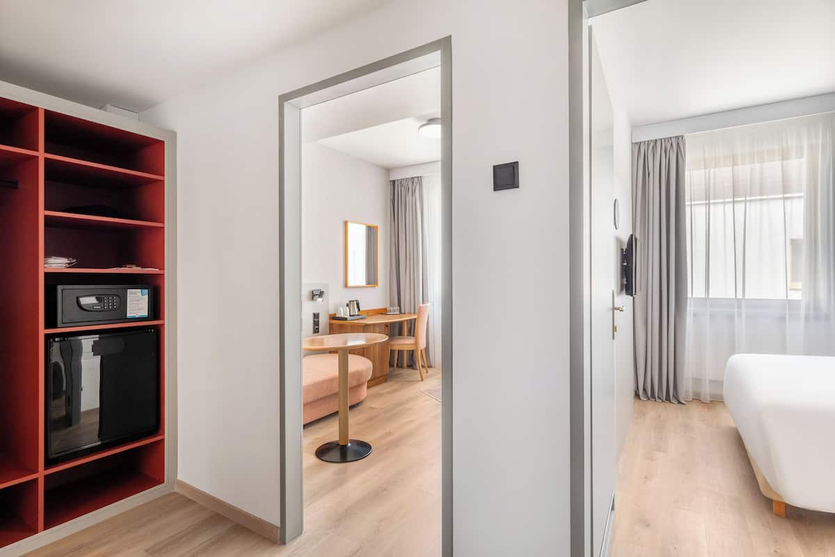 Una habitación de hotel con una cama, un escritorio, una silla, un sofá y un armario con estantes.
