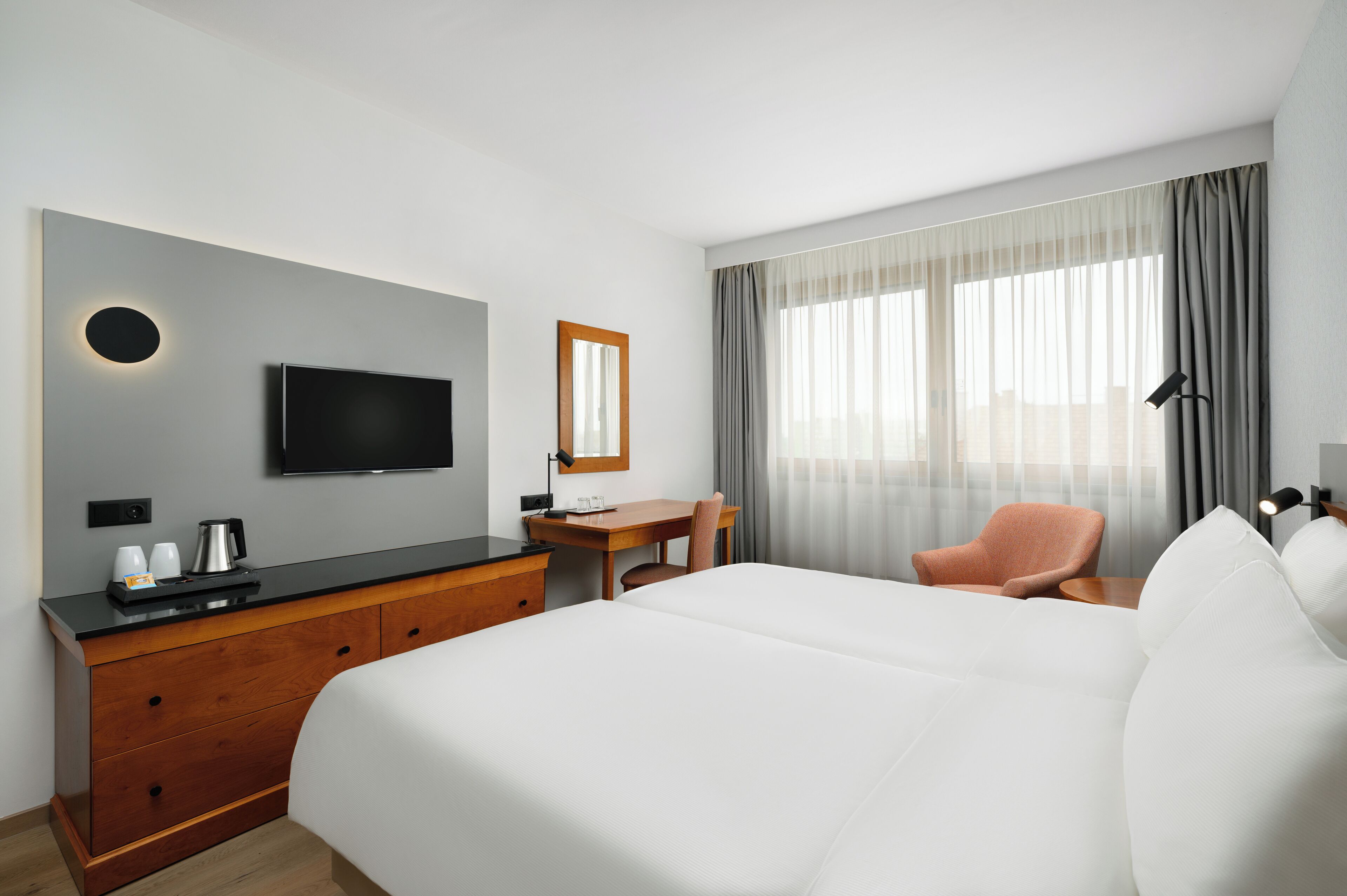 A hotel room with a large bed, a desk with a chair, a television mounted on the wall, and a window with curtains.