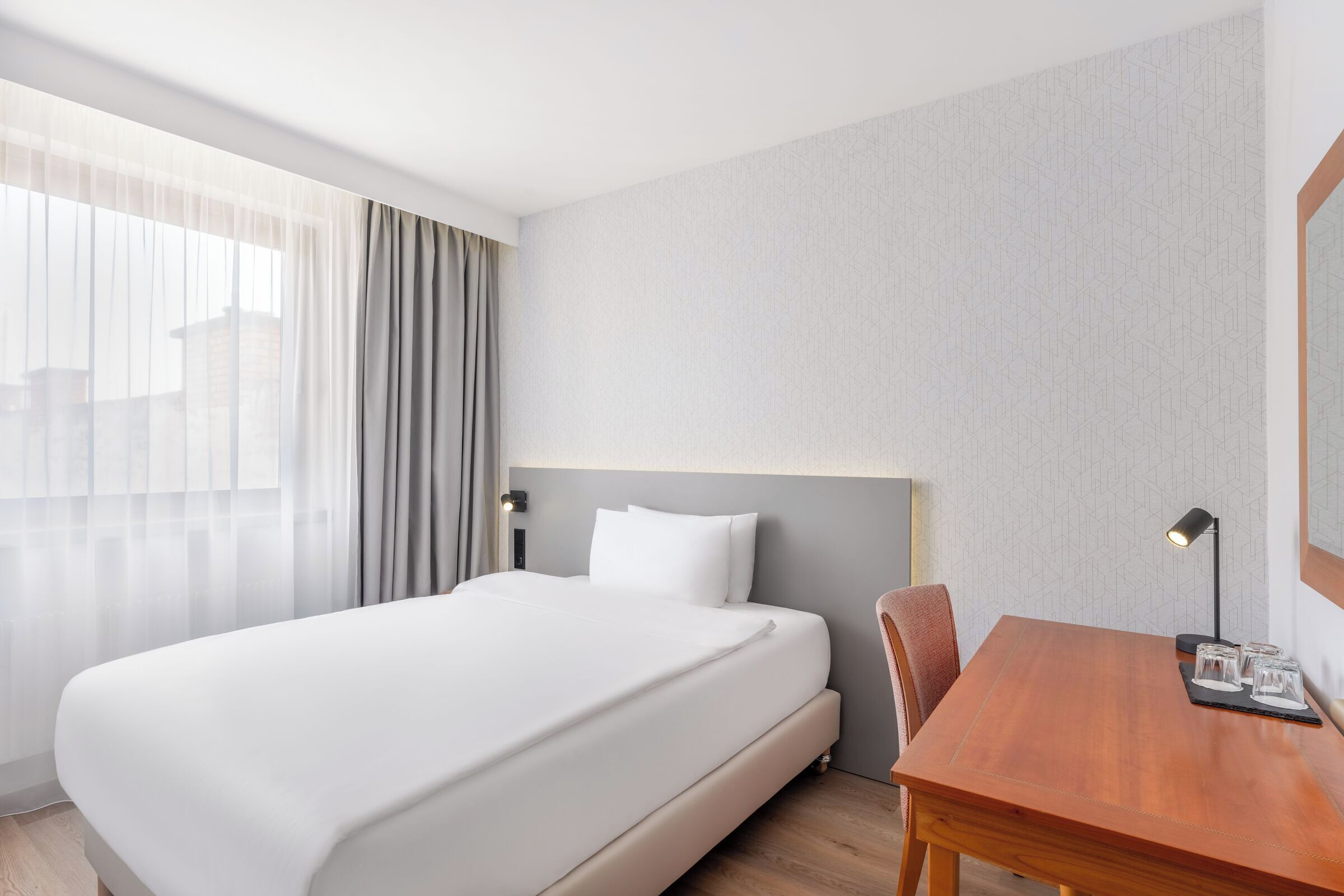 Una camera d'albergo con un letto grande, una scrivania in legno e una sedia.