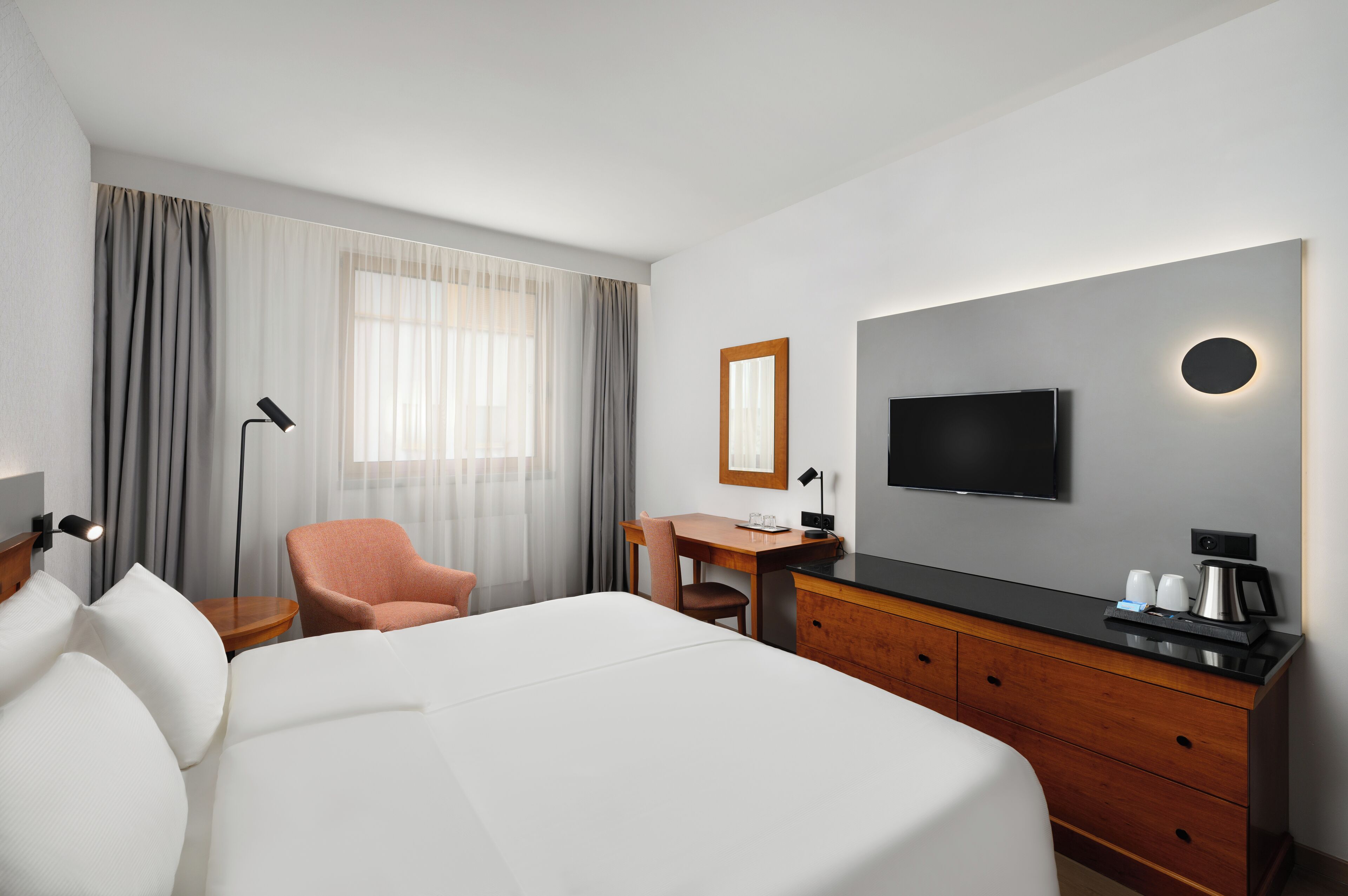 Habitación de hotel con cama, escritorio, silla, televisión y cafetera.