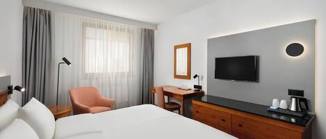 Habitación de hotel con cama, escritorio, silla, televisión y cafetera.