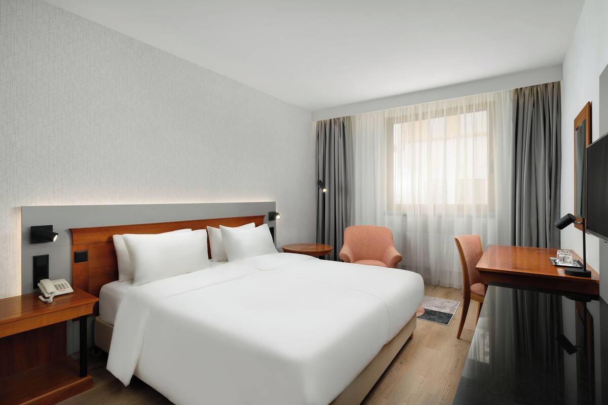 Una habitación de hotel con una cama grande, un escritorio, una silla, un teléfono y una televisión.
