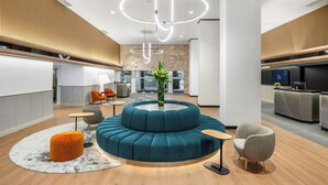 Un hall d’entrée moderne avec un espace salon circulaire, un comptoir d’accueil et une cuisine en arrière-plan.