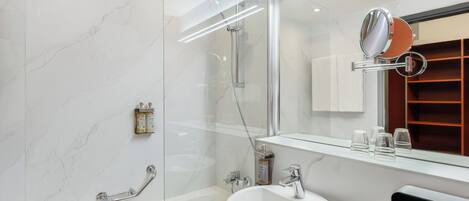 A modern bathroom with a glass-enclosed shower, a white sink, and a large mirror.