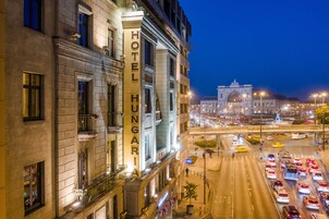 Ένα ξενοδοχείο με μια μεγάλη, επιβλητική επιγραφή που γράφει «HOTEL HUNGARIA», μια πολυσύχναστη διασταύρωση και ένα ιστορικό κτίριο στο βάθος.