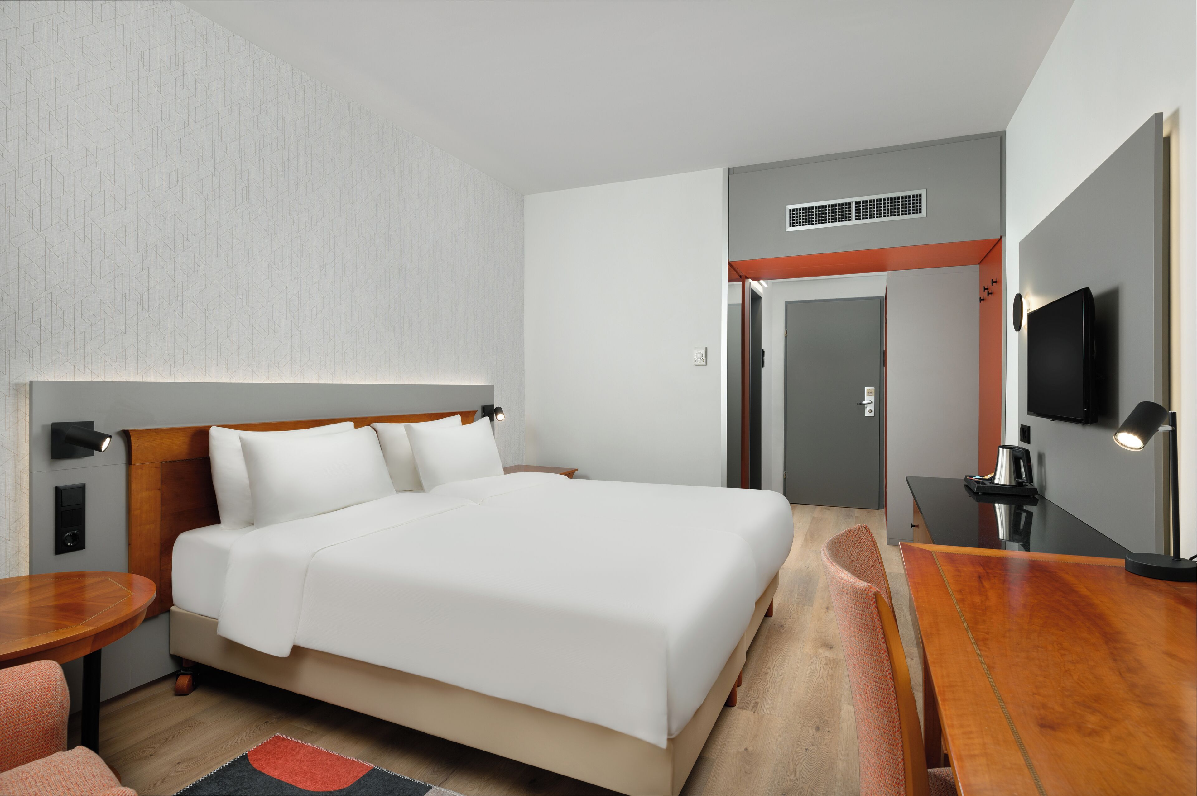 A hotel room with a large bed, a desk, a chair, a TV, and a door.