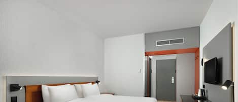 A hotel room with a large bed, a desk, a chair, a TV, and a door.