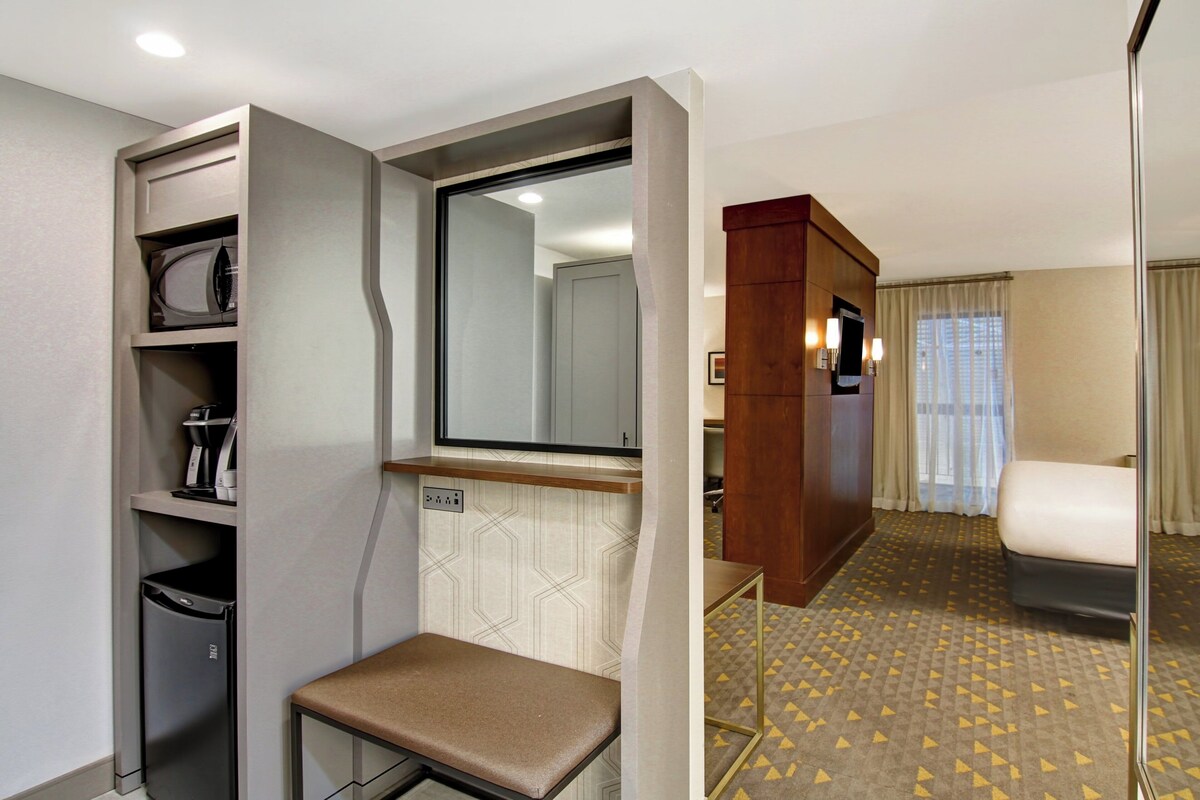 A hotel room with a bed, a seating area, a small kitchenette, and a bathroom.