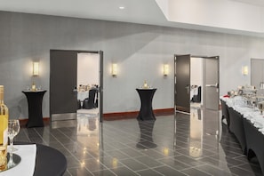 A modern hotel lobby with a polished tile floor, black round tables, and a buffet area with a long counter.