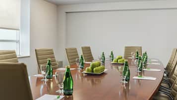 A conference room with a long table, beige chairs, green bottles, glasses, and a plate of green apples.
